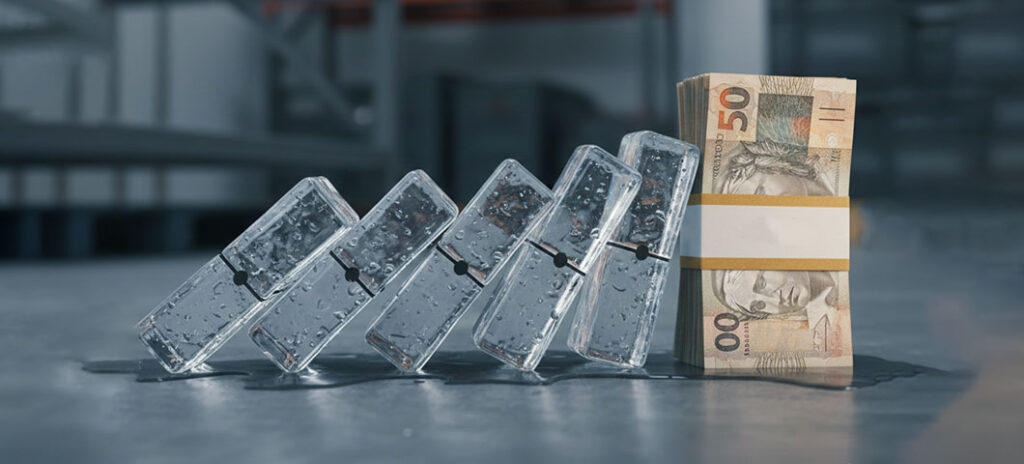 Uma fileira de cubos de gelo perfeitamente alinhados começando a derreter e cair como peças de dominó. O último "dominó" da fila não é um cubo de gelo, mas um maço de notas de dinheiro